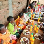 Enfants attablés devant leurs assiettes et jus de fruits à l'école d'Okana
