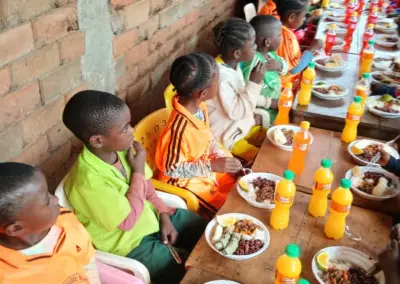 Enfants attablés devant leurs assiettes et jus de fruits à l'école d'Okana